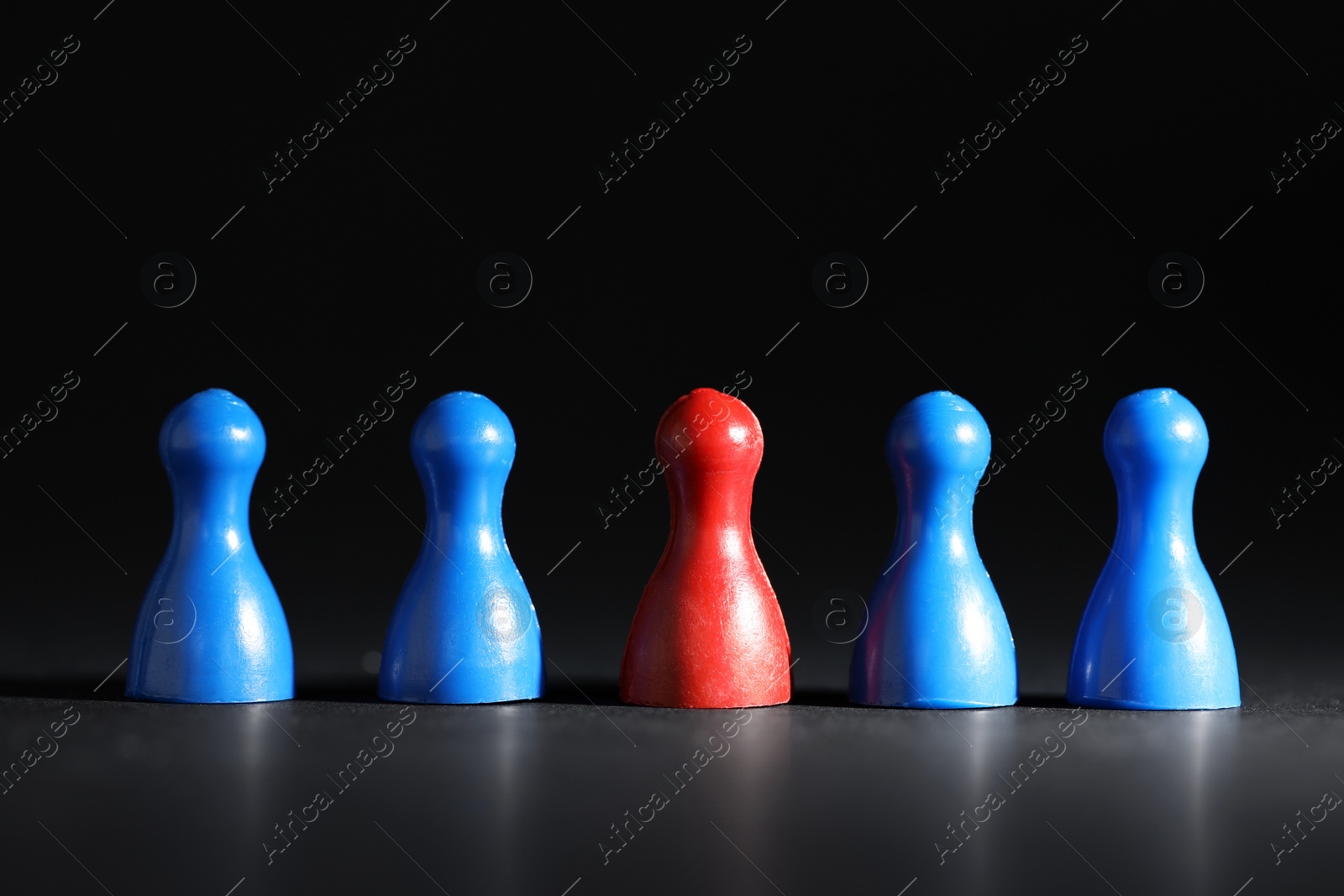 Photo of Choice concept. Red pawn among blue ones on black table, closeup