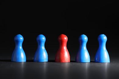 Photo of Choice concept. Red pawn among blue ones on black table, closeup