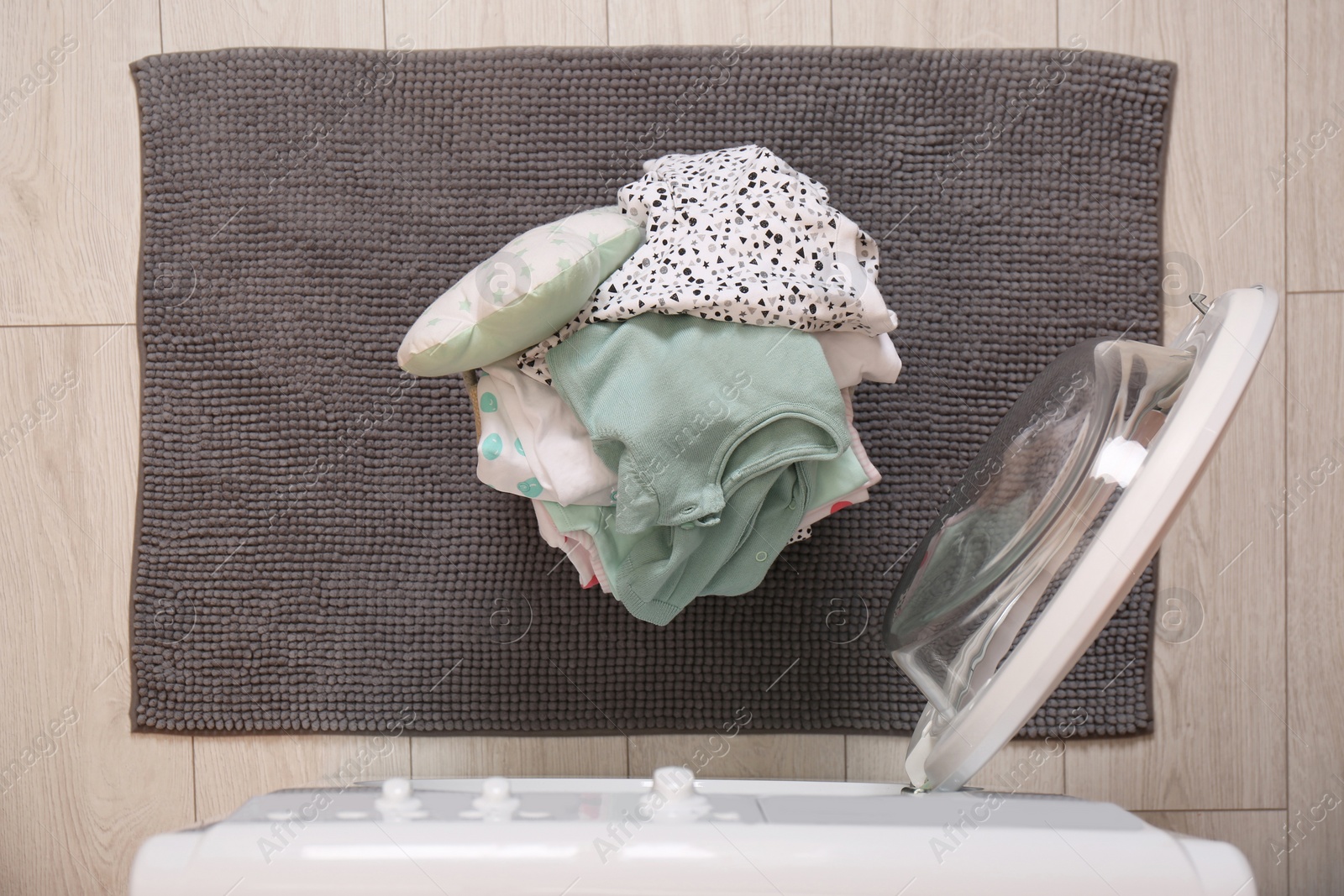 Photo of Laundry basket with baby clothes and bedding near washing machine in bathroom, top view