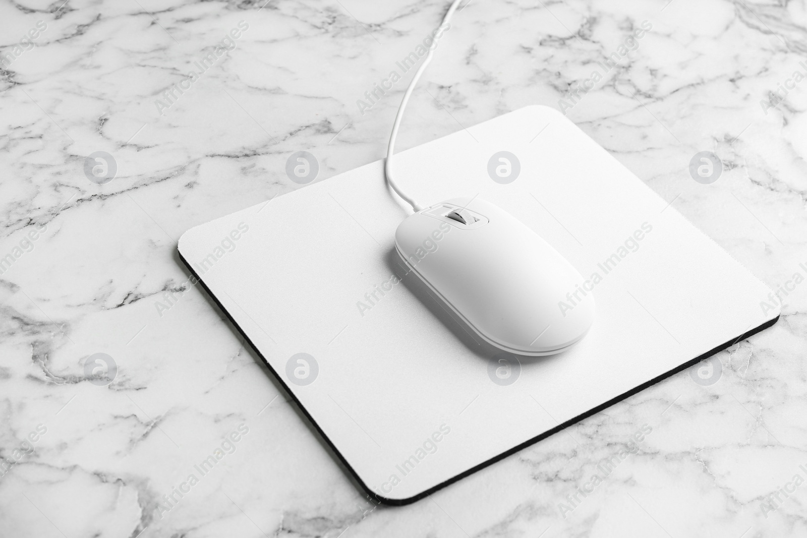 Photo of Modern wired optical mouse and pad on white marble table