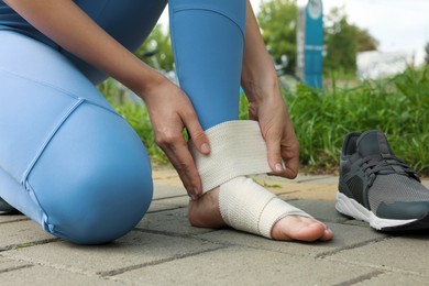 Photo of Woman wrapping foot in medical bandage outdoors, closeup