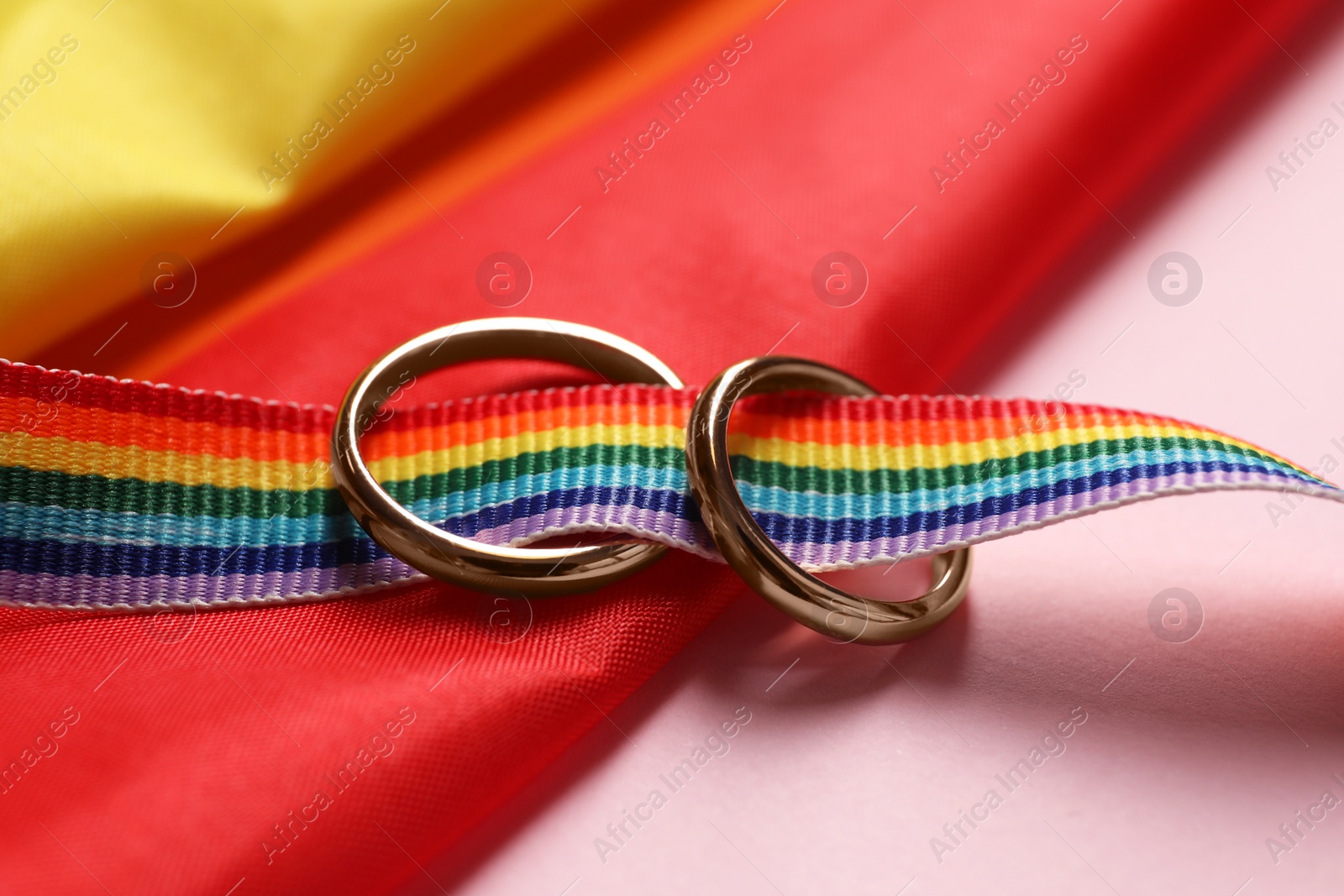 Photo of Rainbow LGBT flag and wedding rings on pink background, closeup