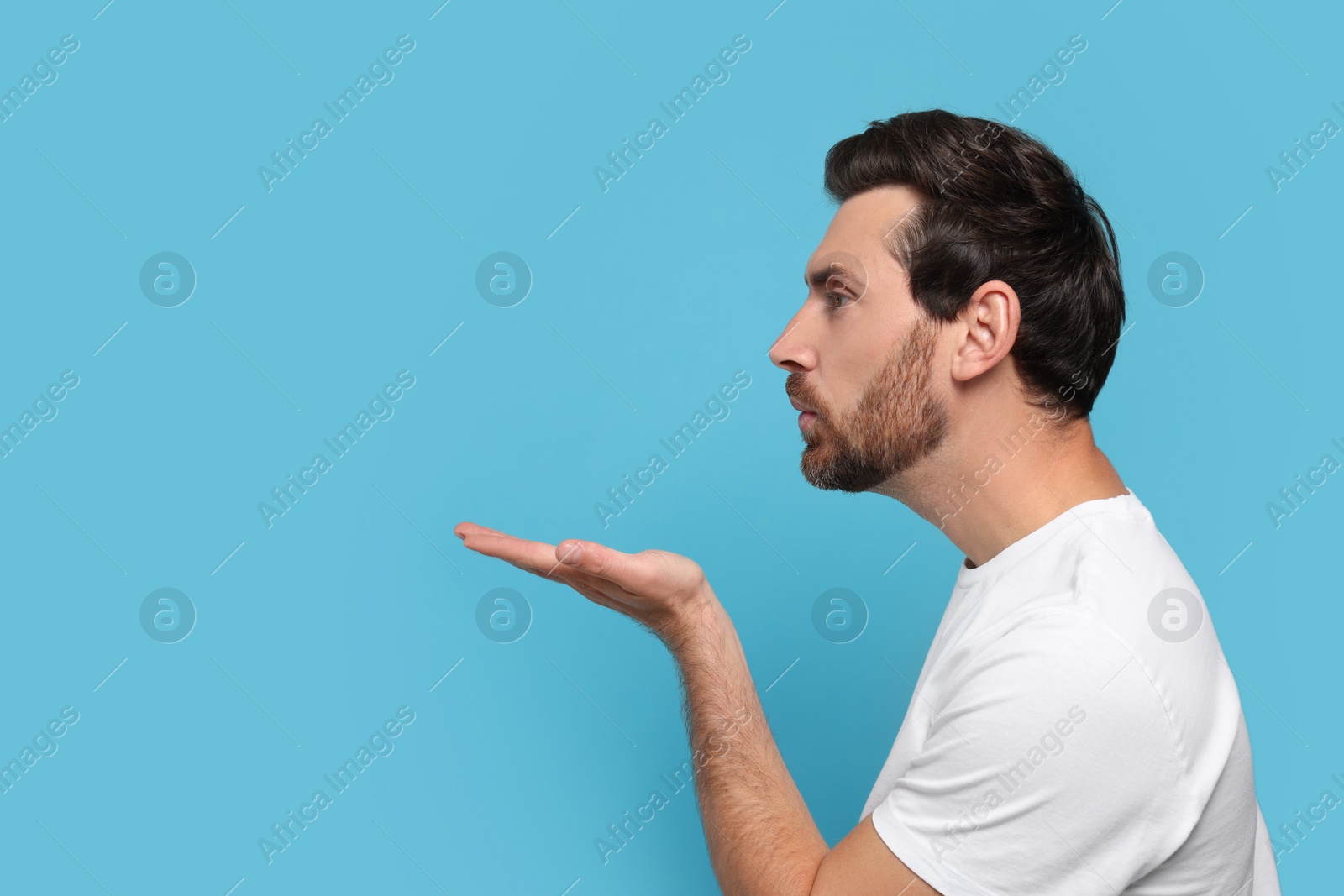 Photo of Handsome man blowing kiss on light blue background. Space for text