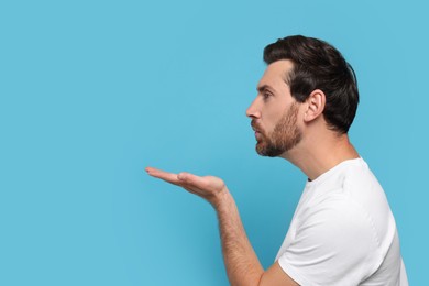 Handsome man blowing kiss on light blue background. Space for text