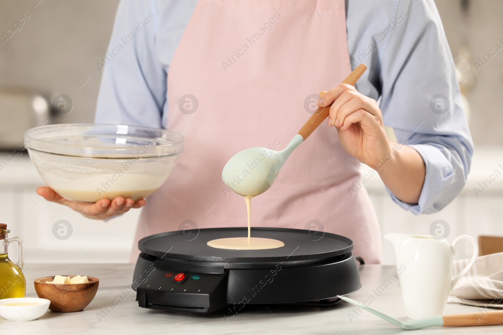 Photo of Woman cooking delicious crepe on electric pancake maker at white marble table in kitchen, closeup