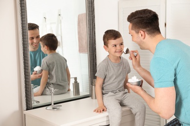 Photo of Dad applying shaving foam onto son's face in bathroom