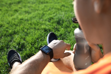 Photo of Man checking fitness tracker after training in park, closeup