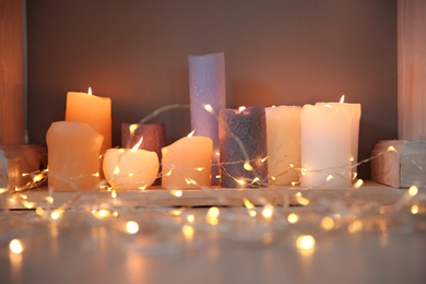 Photo of Burning candles and Christmas lights on floor indoors
