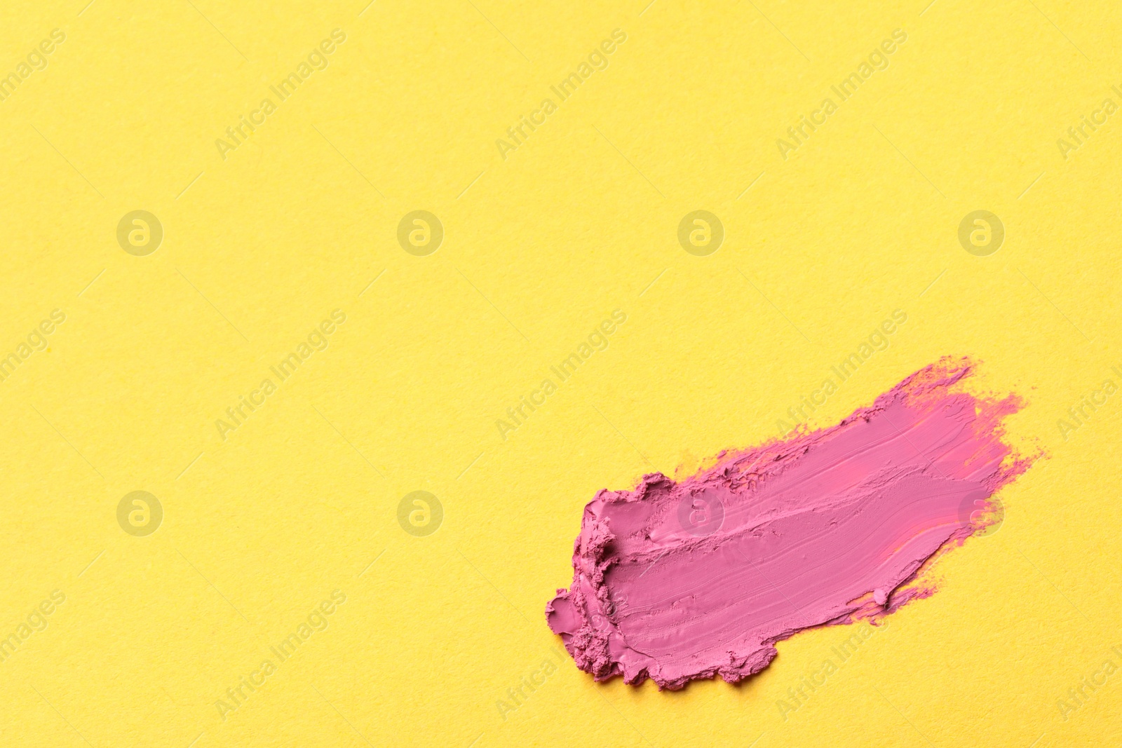 Photo of Smear of bright lipstick on yellow background, top view