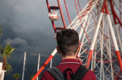 Teenage boy near large Ferris wheel outdoors, back view. Space for text
