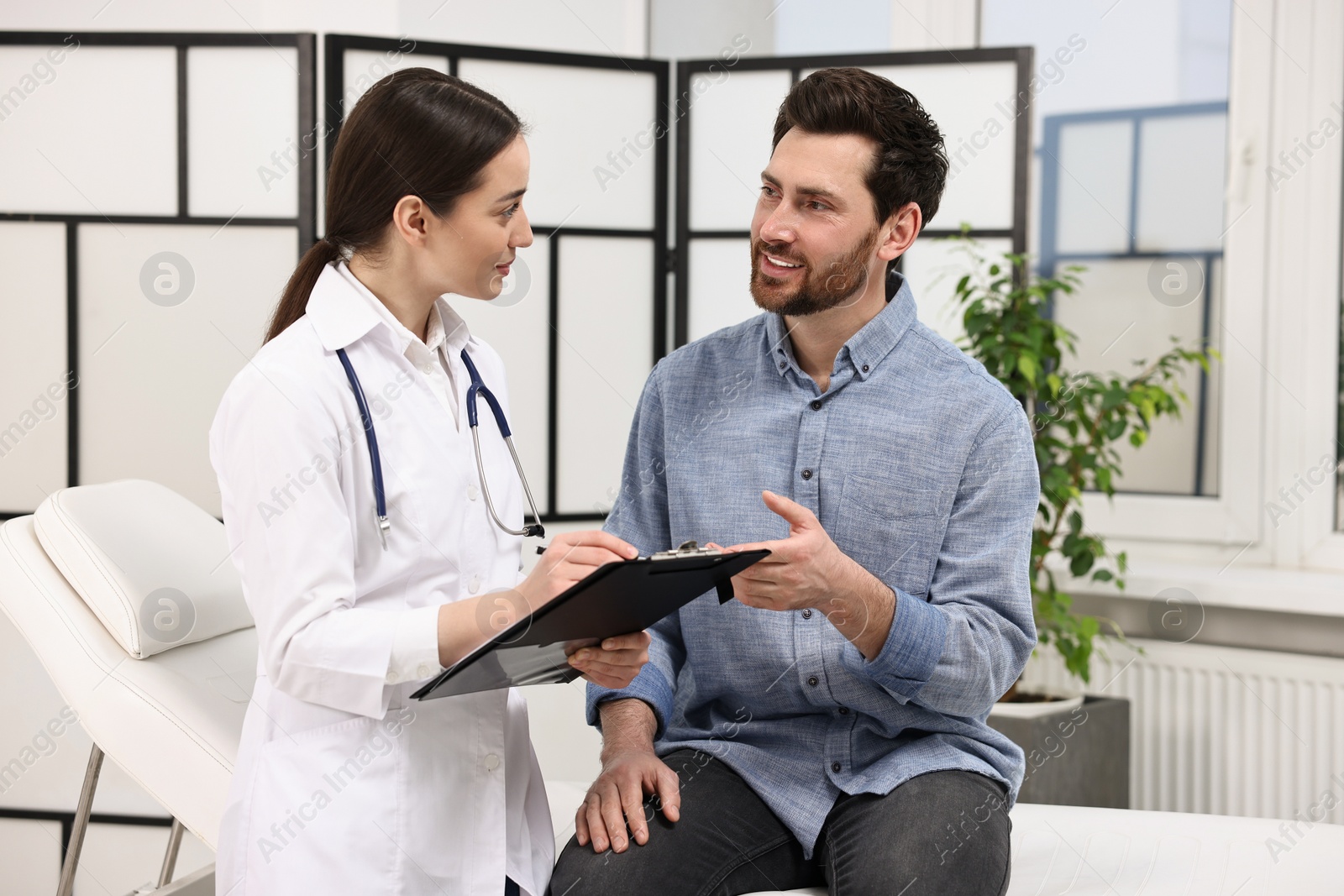 Photo of Doctor with clipboard consulting patient during appointment in clinic