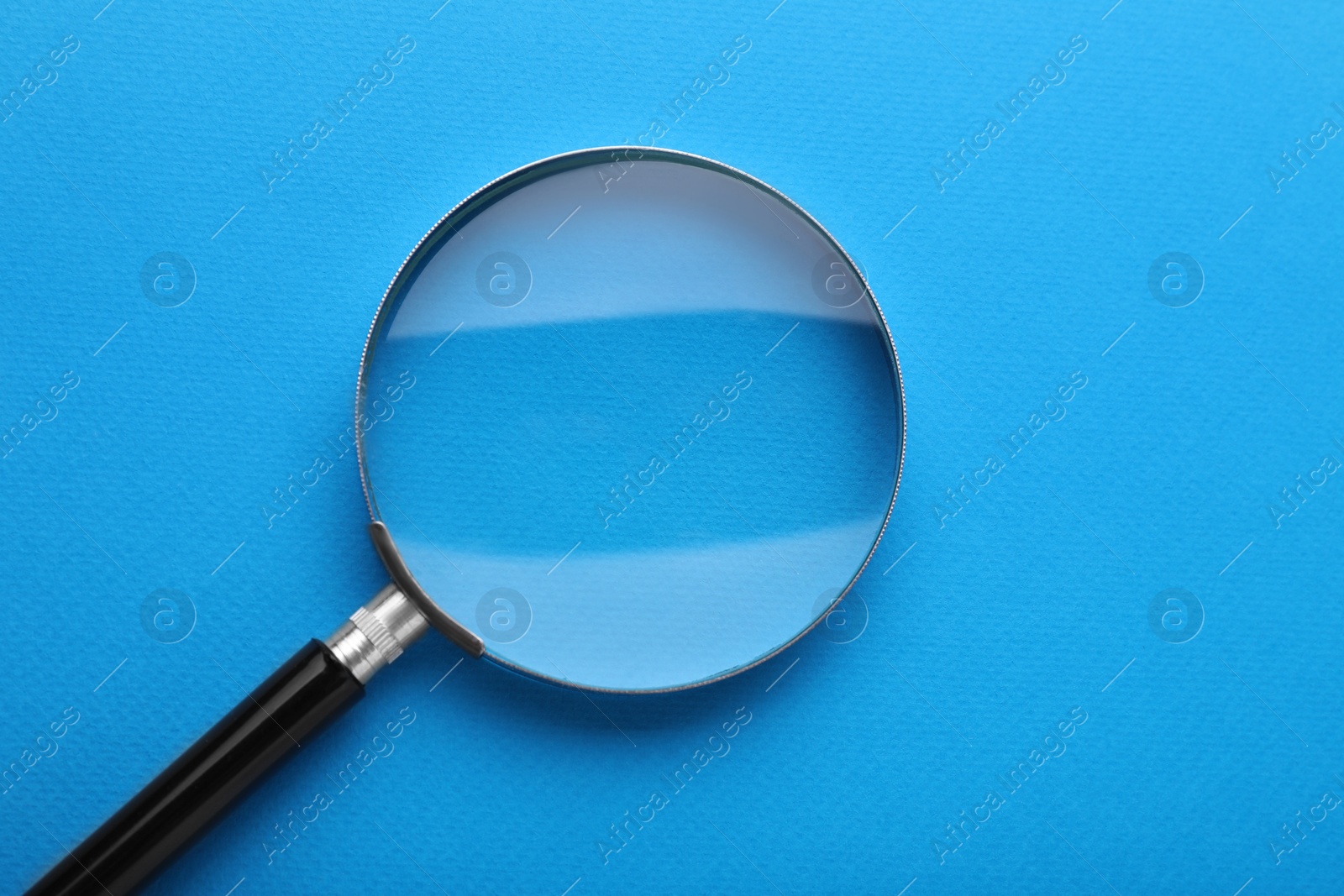 Photo of Magnifying glass on light blue background, top view