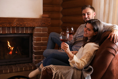 Photo of Lovely couple with glasses of wine resting near fireplace at home. Winter vacation