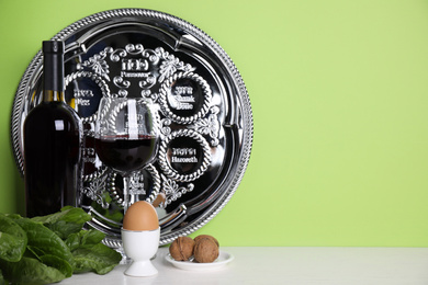 Photo of Symbolic Pesach (Passover Seder) items on wooden table against green background, space for text