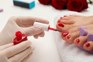 Photo of Pedicurist painting client`s toenails with red polish in beauty salon, closeup