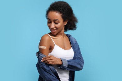 Photo of Young woman with adhesive bandage on her arm after vaccination against light blue background
