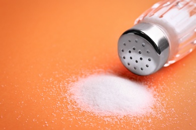 Photo of Scattered salt and shaker on orange background, closeup. Space for text