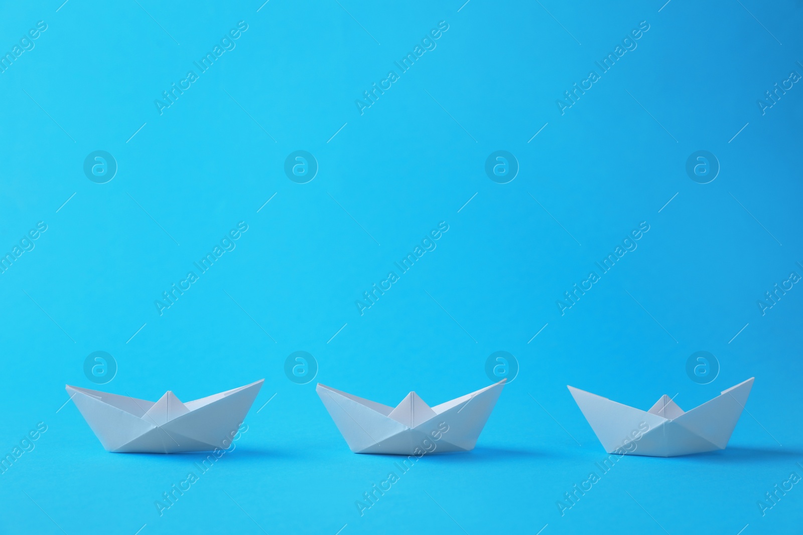 Photo of Handmade white paper boats on light blue background. Origami art