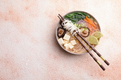 Photo of Bowl of vegetarian ramen and chopsticks on color textured table, top view. Space for text