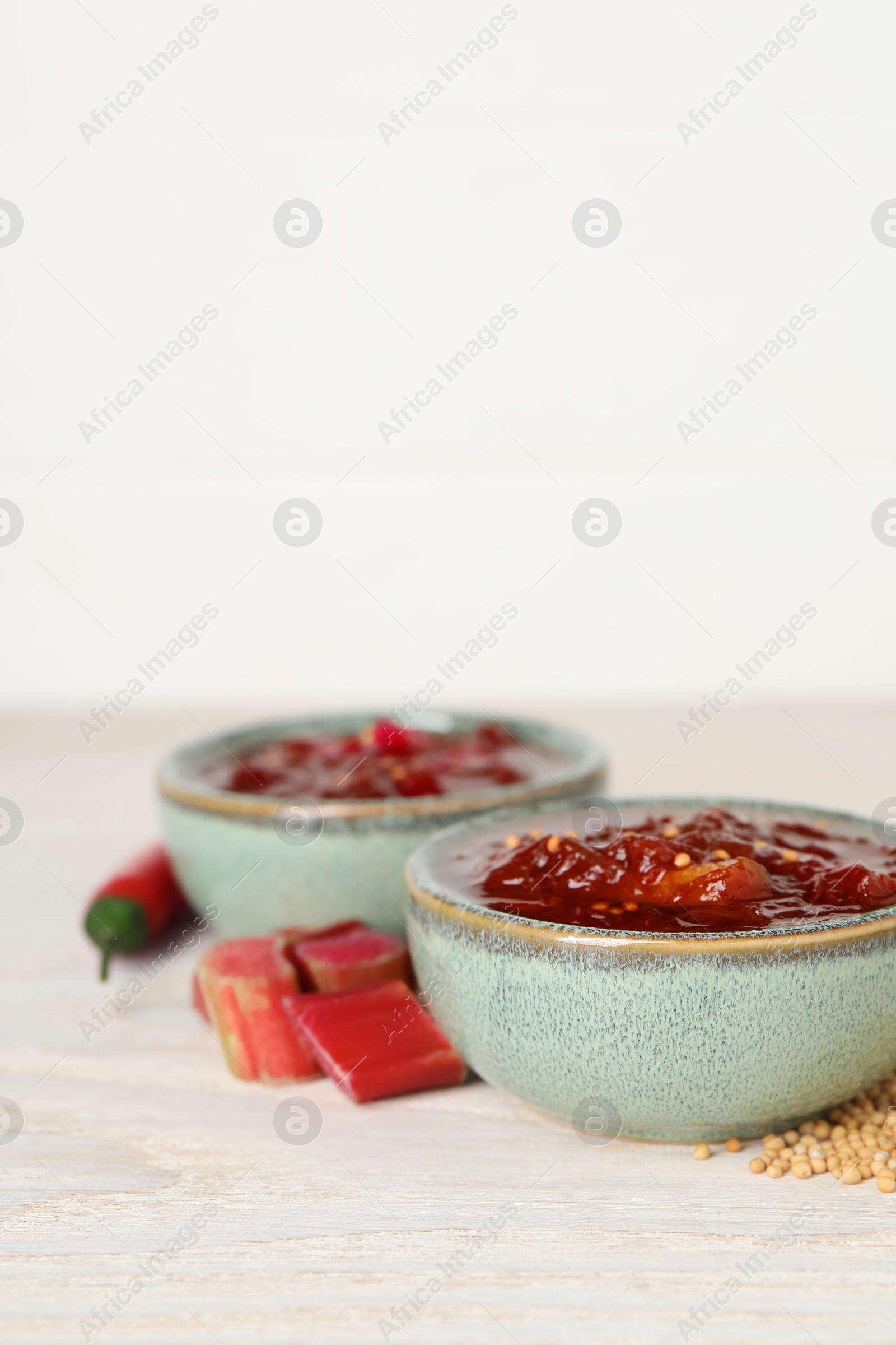 Photo of Tasty rhubarb sauce and ingredients on white wooden table, closeup. Space for text