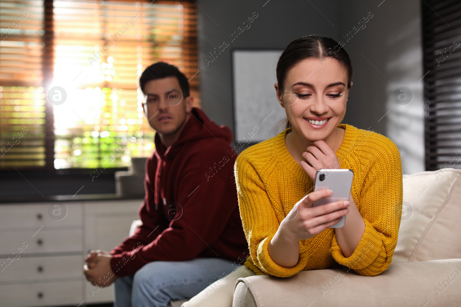 Photo of Distrustful man peering into girlfriend's smartphone at home. Jealousy in relationship