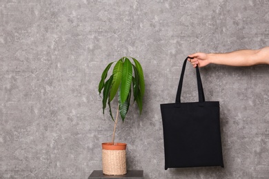 Photo of Young man holding eco bag at table with potted plant near grey wall