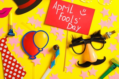 Photo of Sign with phrase April Fools' Day and different clown's accessories on yellow background, flat lay