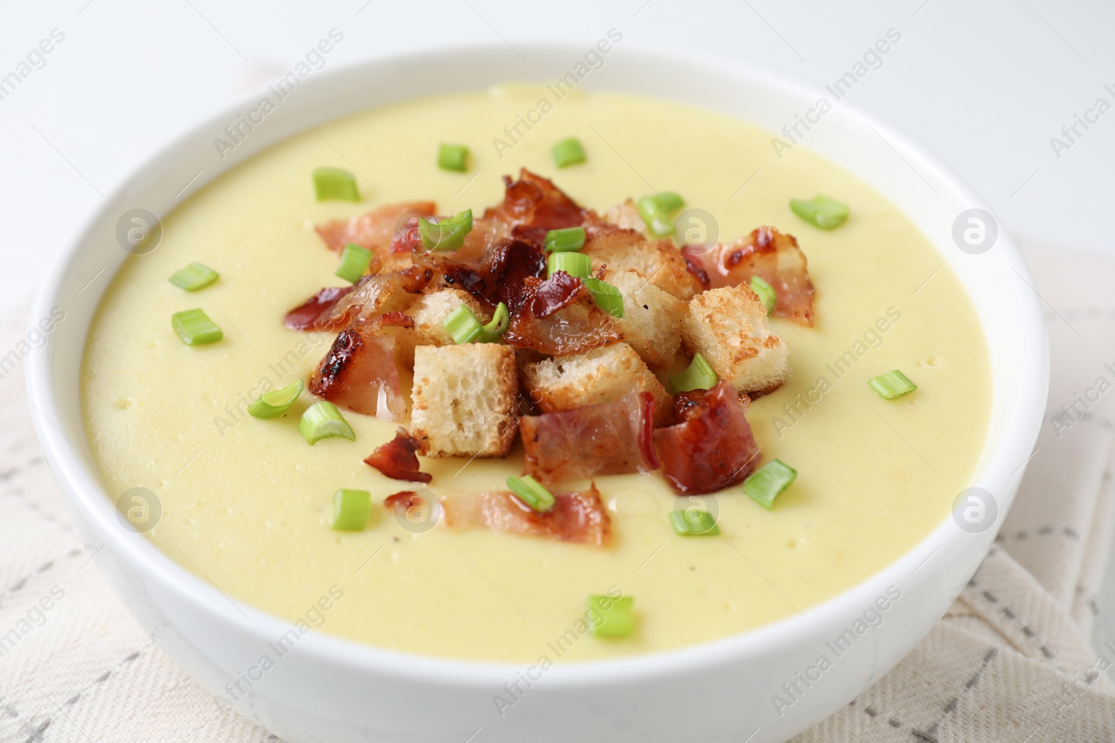 Photo of Tasty potato soup with bacon, green onion and croutons in bowl on white table, closeup