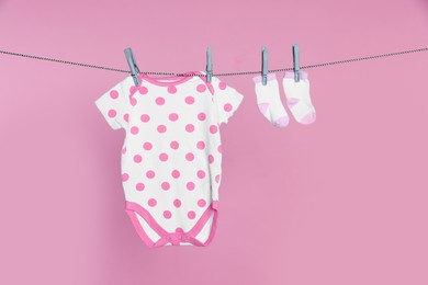 Baby onesie and socks drying on laundry line against pink background