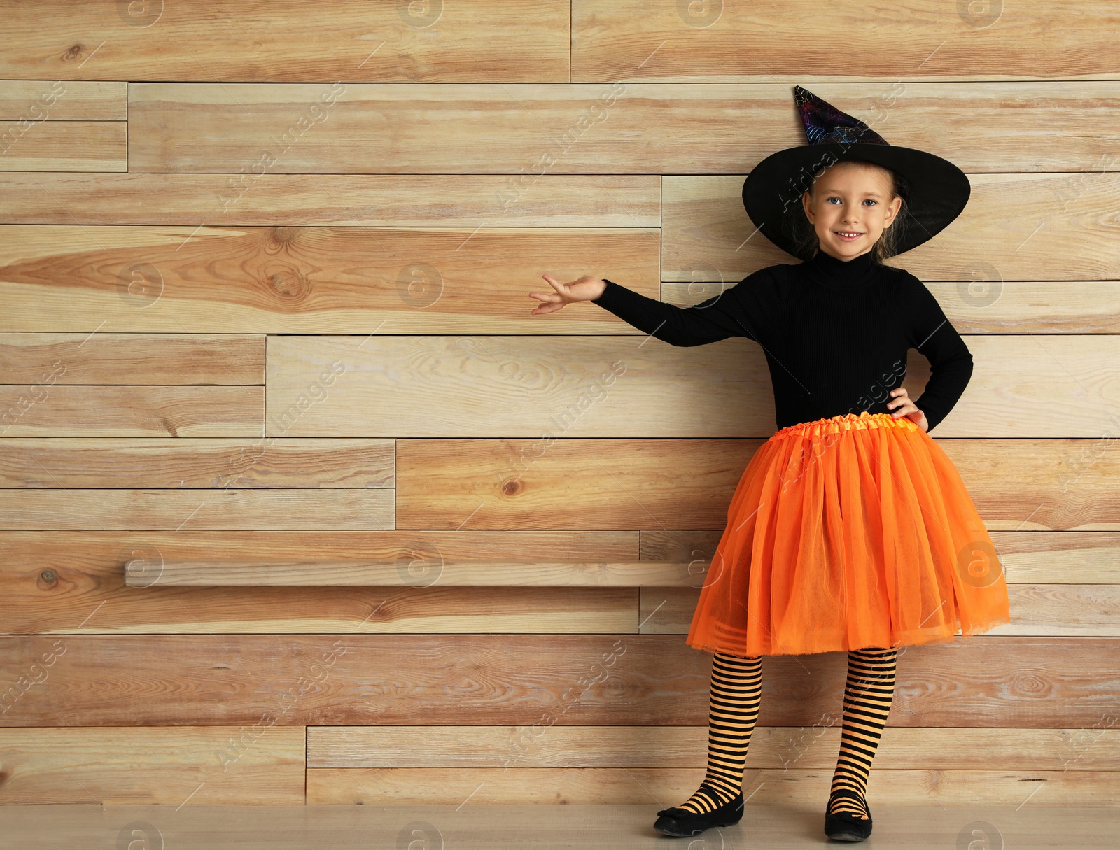 Photo of Cute little girl wearing Halloween costume near wooden wall. Space for text