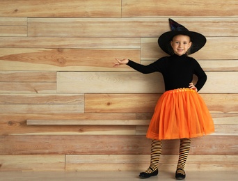 Cute little girl wearing Halloween costume near wooden wall. Space for text