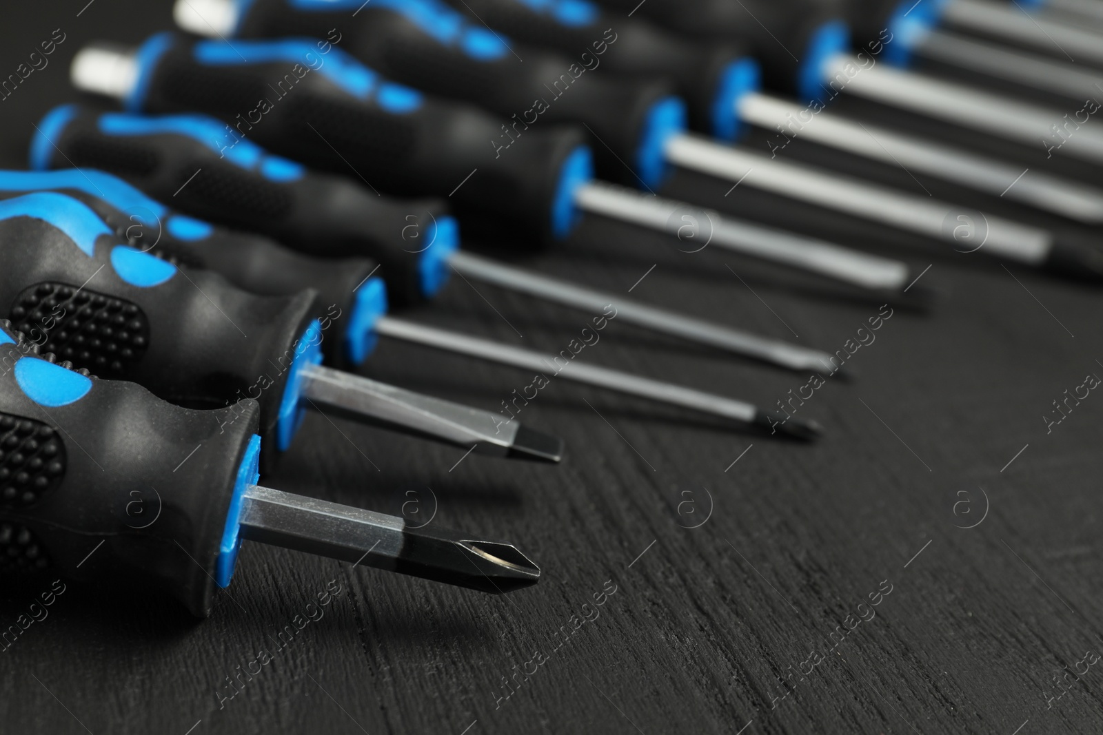 Photo of Set of screwdrivers on black wooden table, closeup