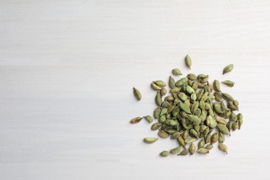 Pile of dry cardamom pods on white wooden table, top view. Space for text