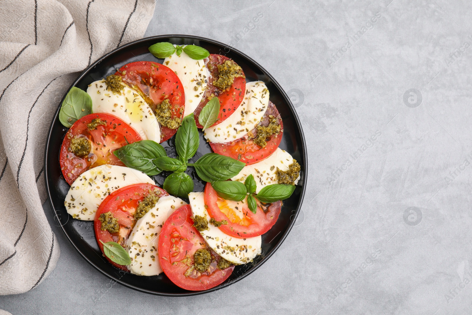 Photo of Plate of delicious Caprese salad with pesto sauce on grey table, top view. Space for text