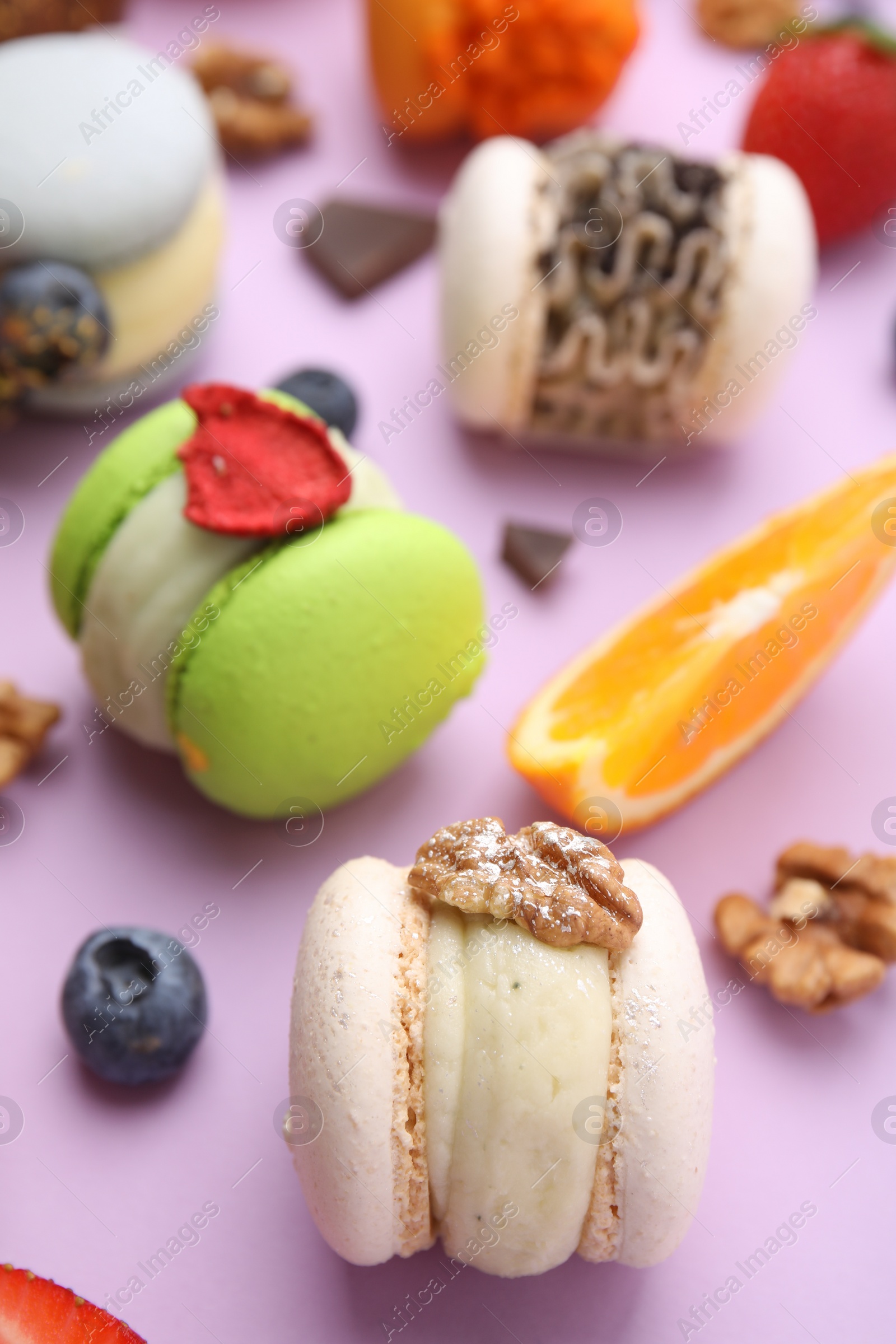 Photo of Delicious macarons, orange and berries on violet table, closeup
