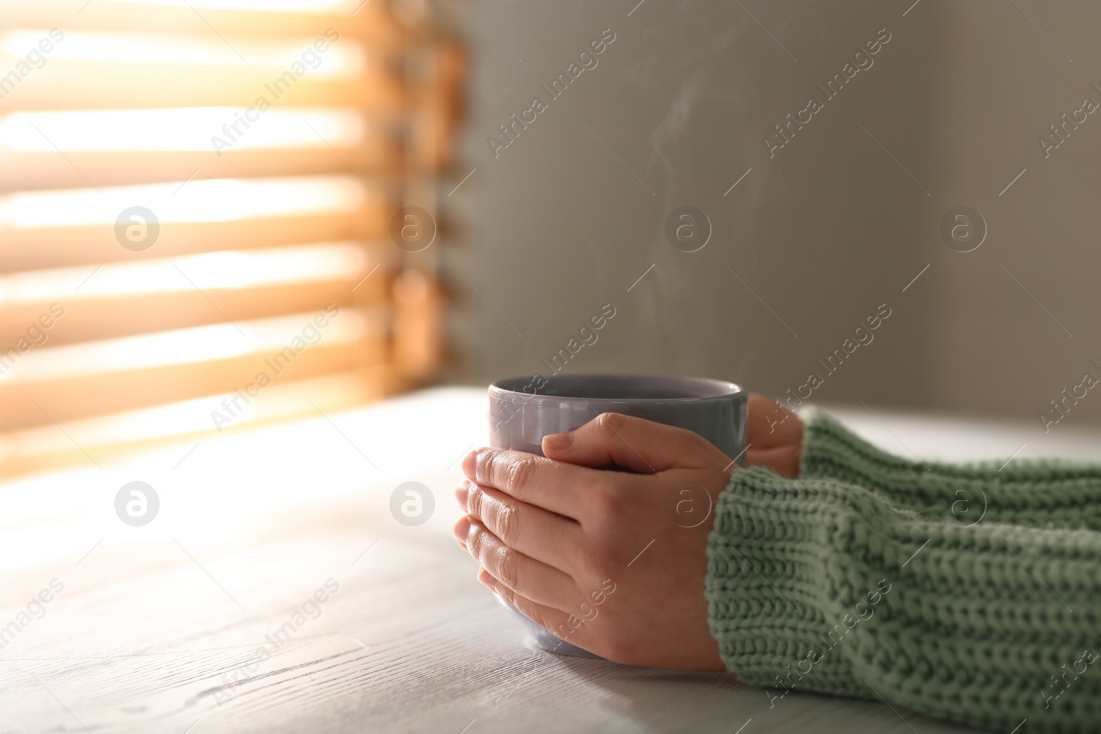 Photo of Woman with cup of tasty coffee at white wooden table, closeup. Good morning