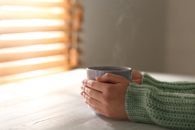 Photo of Woman with cup of tasty coffee at white wooden table, closeup. Good morning