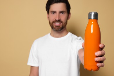Man with orange thermo bottle against beige background, space for text. Focus on hand