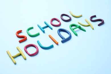 Photo of Phrase School Holidays made of modeling clay on light blue background