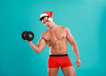 Sexy shirtless Santa Claus with dumbbell on blue background
