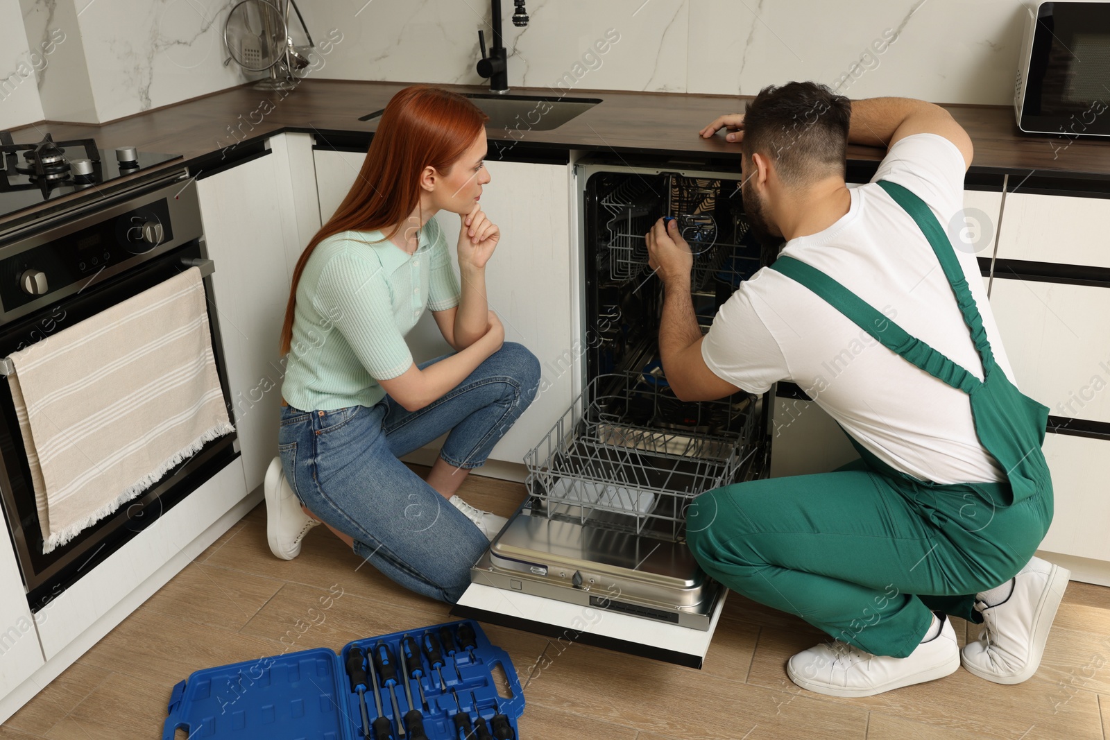 Photo of Woman looking how serviceman repairing her dishwasher in kitchen