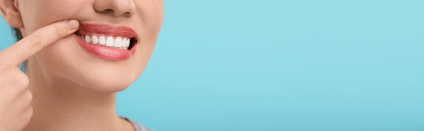 Image of Woman showing her clean teeth on light blue background, closeup. Banner design with space for text