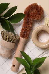 Photo of Cleaning brushes, towel and green leaves on beige background, top view