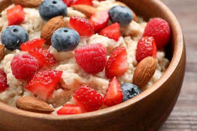 Photo of Tasty oatmeal porridge with berries and almond nuts in bowl, closeup