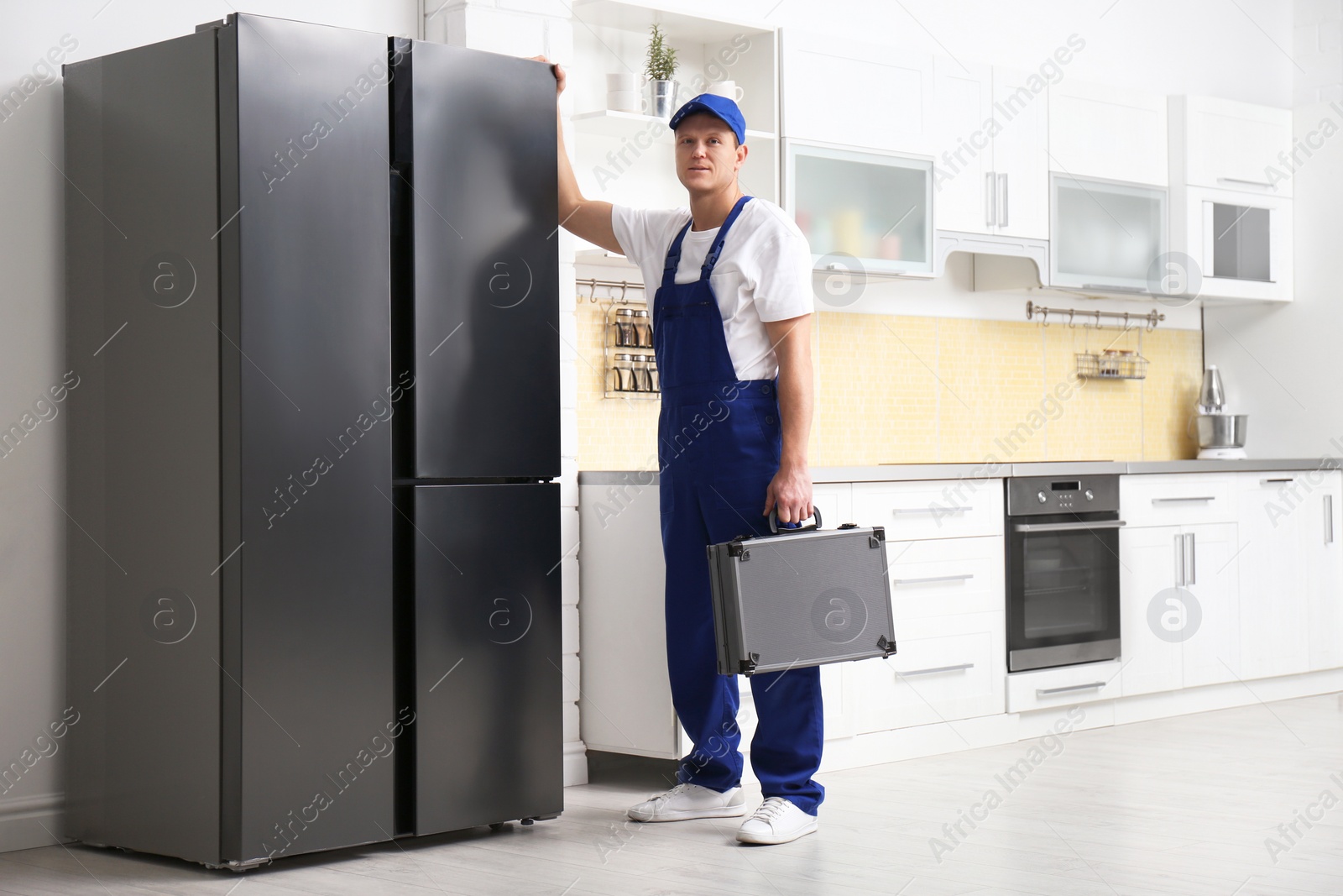 Photo of Male technician with tool box near refrigerator in kitchen