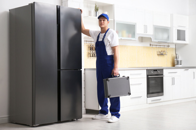 Male technician with tool box near refrigerator in kitchen