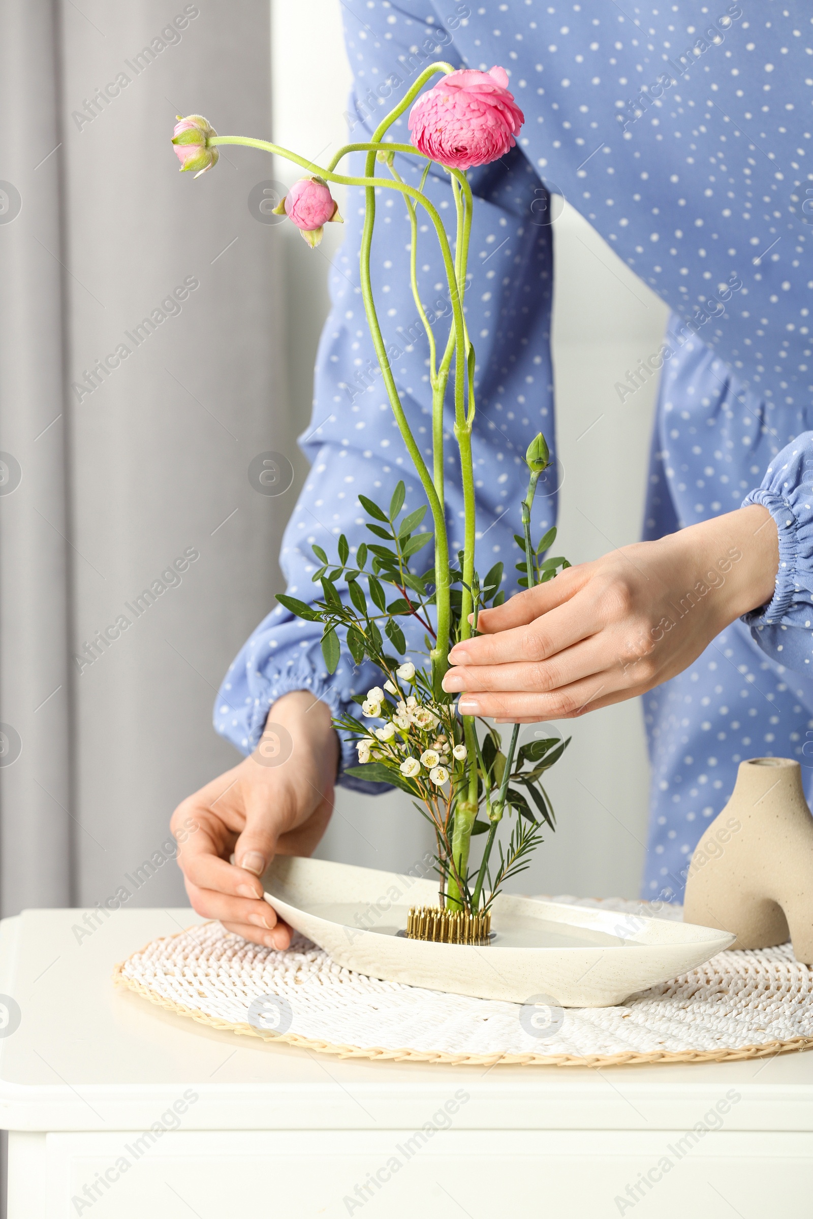 Photo of Woman creating stylish ikebana with beautiful flowers and green branches at white table, closeup