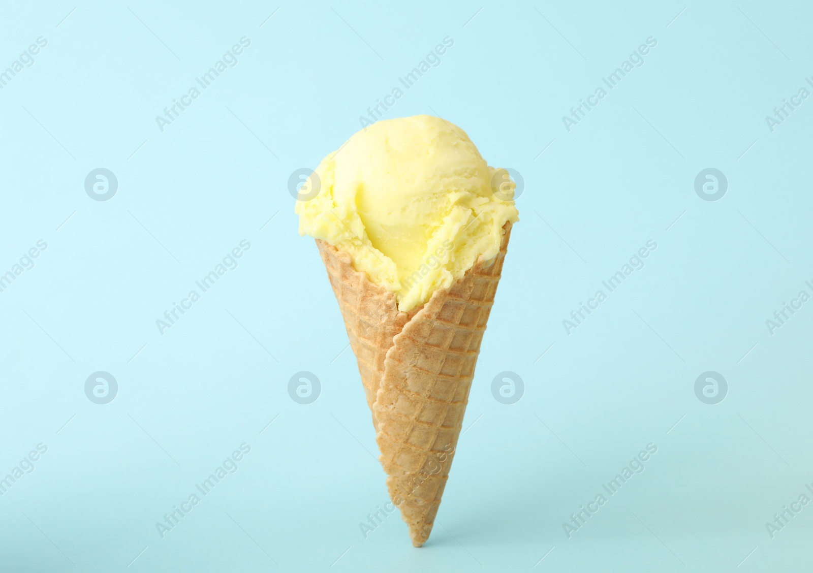 Photo of Delicious yellow ice cream in waffle cone on light blue background