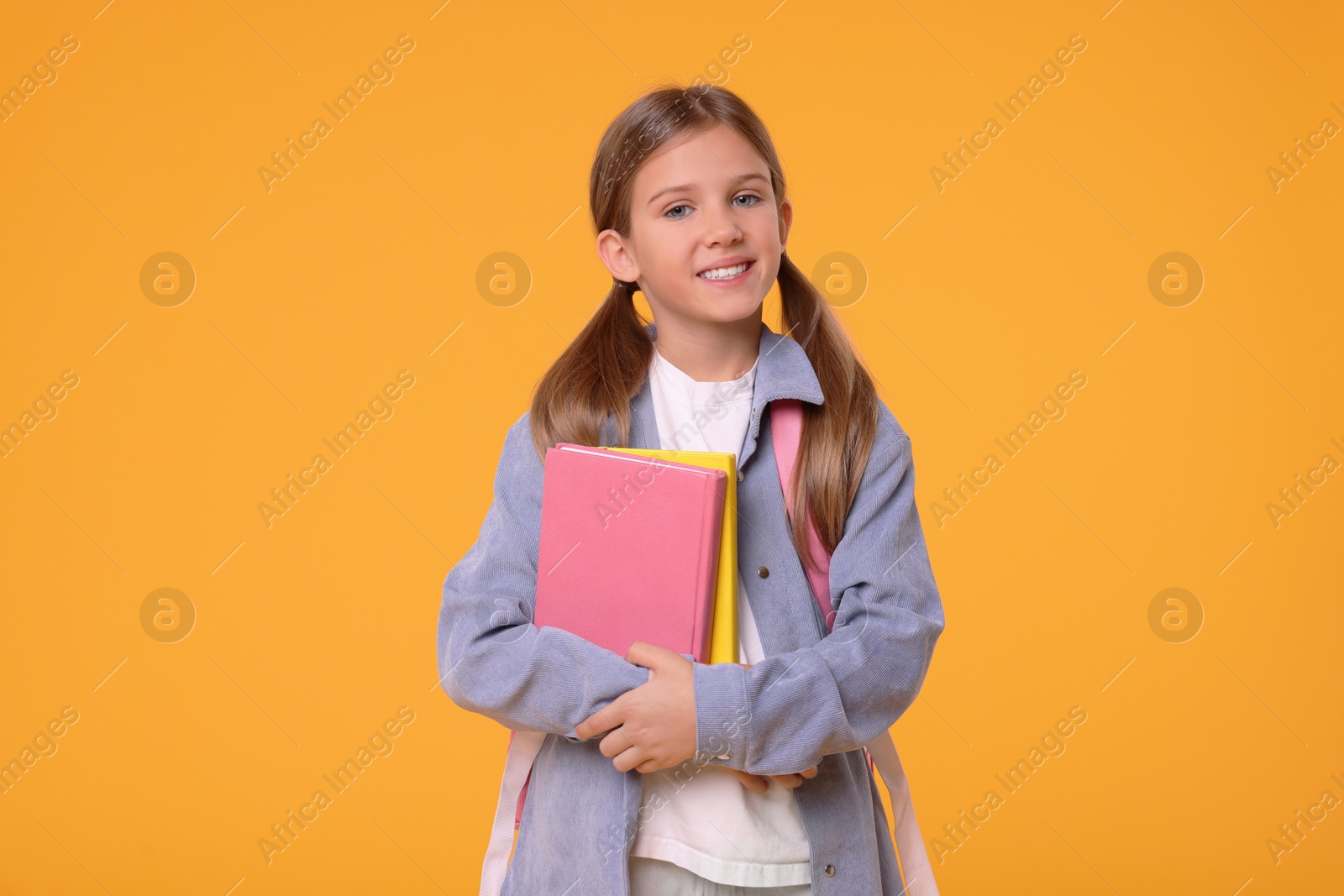 Photo of Happy schoolgirl with books on orange background