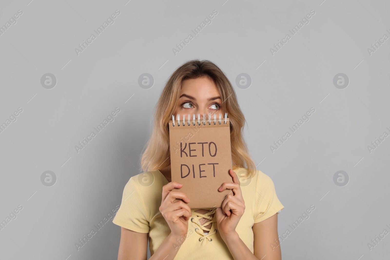 Photo of Woman holding notebook with phrase Keto Diet on grey background